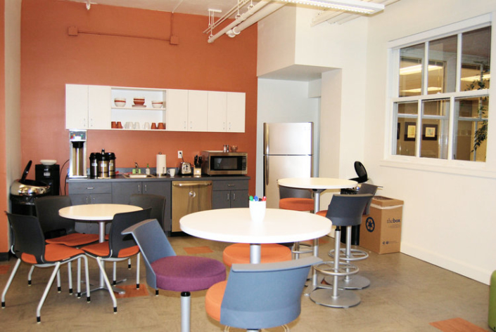 Commercial lunch room with round white tables and cushioned bar stools in assorted colors