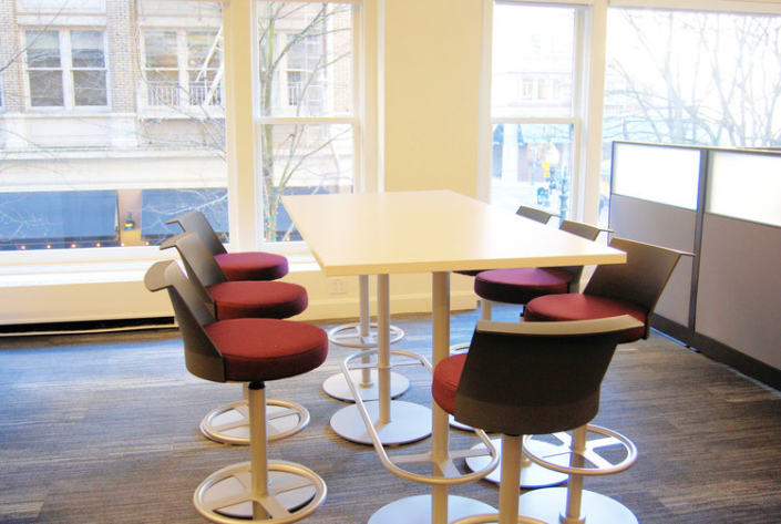 Small standing height conference table with cushioned stools for commercial space