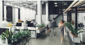 A modern-looking small office with an open layout, multiple workstations, and blurred business colleagues walking around.