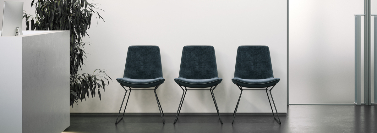 An office reception area with a white wall and dark floors. The reception area also has three chairs and a plant.