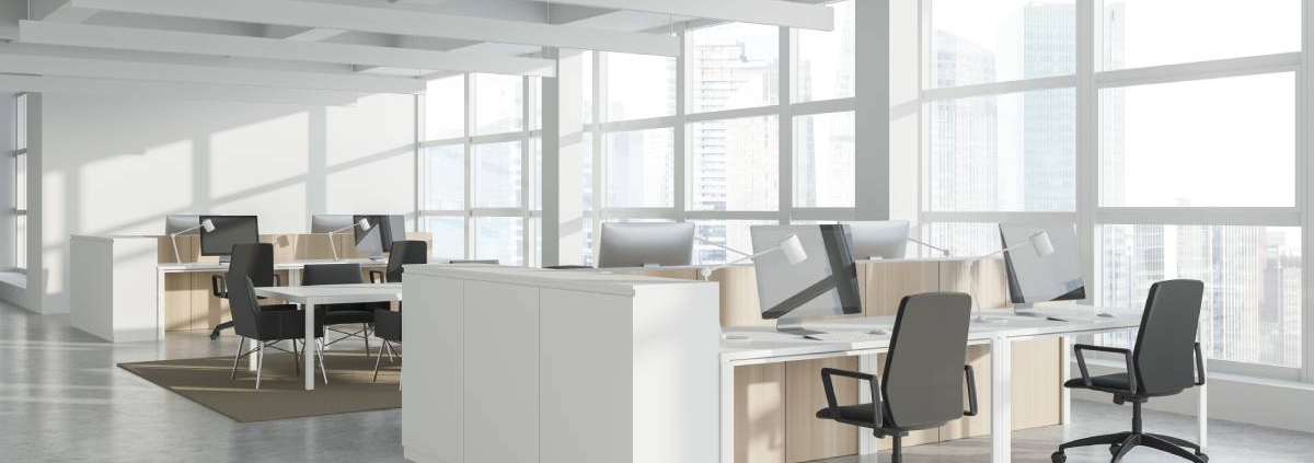 A high-rise office with large windows has a view of various skyscrapers. There are chairs, desks, and monitors in the office.