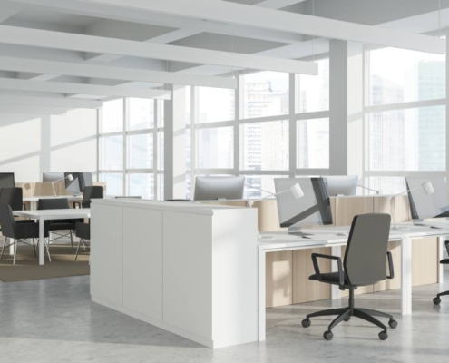 A high-rise office with large windows has a view of various skyscrapers. There are chairs, desks, and monitors in the office.