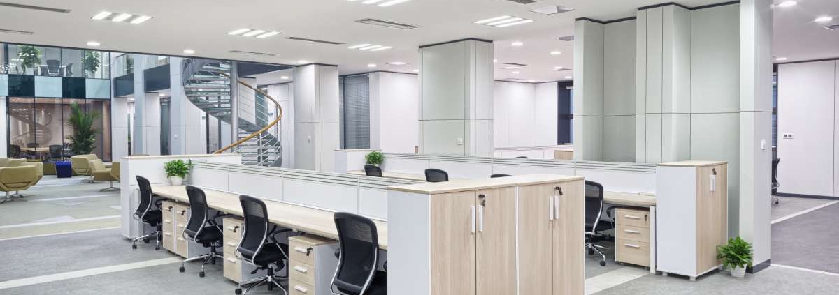 An open and well-lit office space with a spiral staircase, a sitting area, and a long communal desk with chairs and drawers.