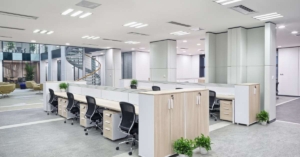 An open and well-lit office space with a spiral staircase, a sitting area, and a long communal desk with chairs and drawers.