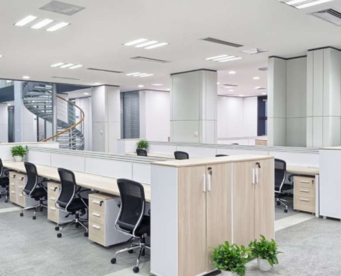 An open and well-lit office space with a spiral staircase, a sitting area, and a long communal desk with chairs and drawers.