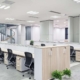 An open and well-lit office space with a spiral staircase, a sitting area, and a long communal desk with chairs and drawers.