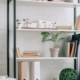 An office with shelves that have books and plants on them. There is also a desk and a chair in the office.