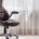 A brown leather office chair in a light-colored room next to a window. The sun is shining through the window.