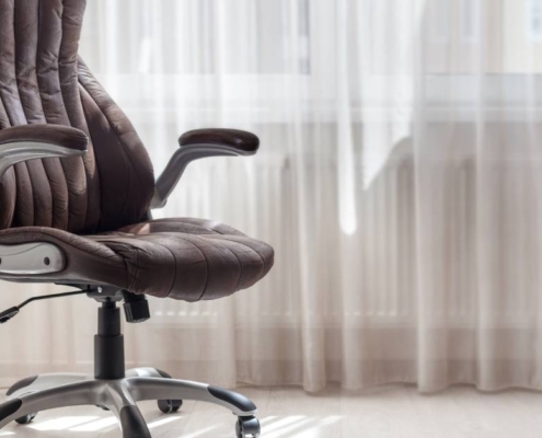 A brown leather office chair in a light-colored room next to a window. The sun is shining through the window.