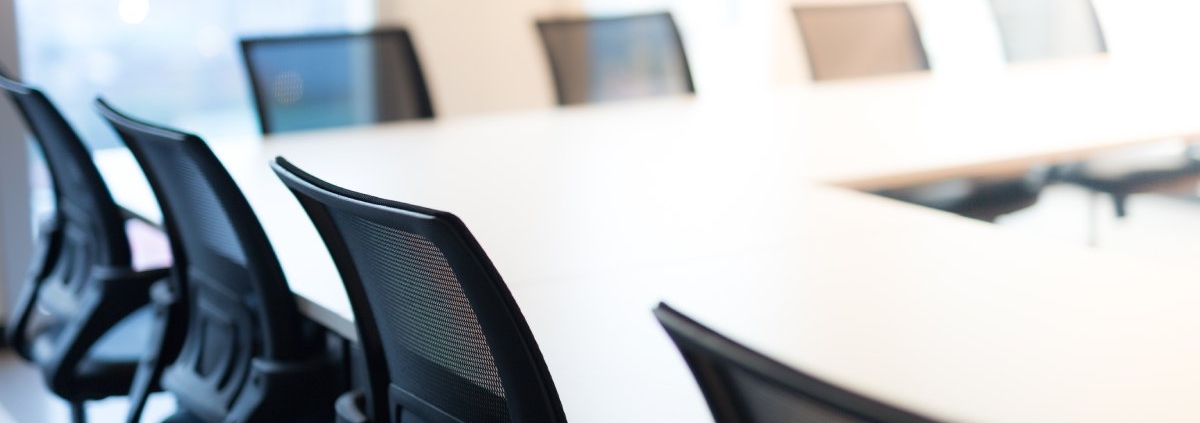 A row of office chairs around a table in a room. The office chairs are black, and there's a window in the background.