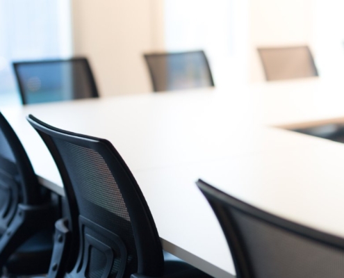 A row of office chairs around a table in a room. The office chairs are black, and there's a window in the background.