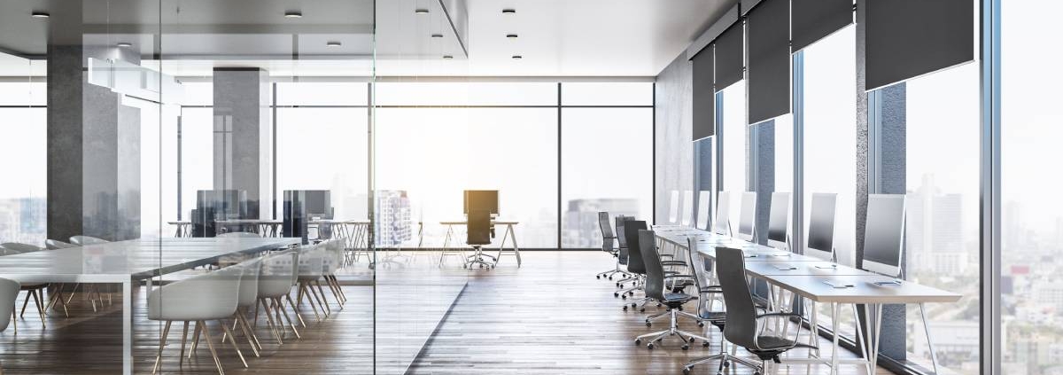 An office that has a row of desks, chairs, and monitors. There's an area with a large table and multiple chairs.