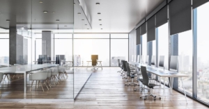 An office that has a row of desks, chairs, and monitors. There's an area with a large table and multiple chairs.