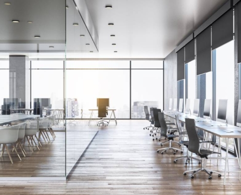 An office that has a row of desks, chairs, and monitors. There's an area with a large table and multiple chairs.