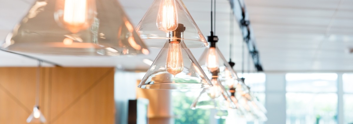 Clear glass pendant ceiling lights are hanging in a line and illuminating a bright, modern office space.