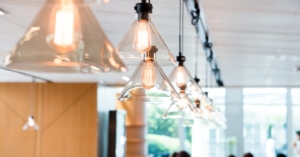Clear glass pendant ceiling lights are hanging in a line and illuminating a bright, modern office space.