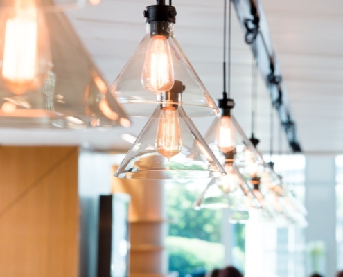 Clear glass pendant ceiling lights are hanging in a line and illuminating a bright, modern office space.