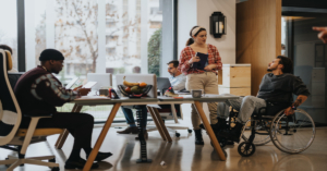 A diverse office team collaborates in an inclusive workspace, with one member in a wheelchair using a laptop.