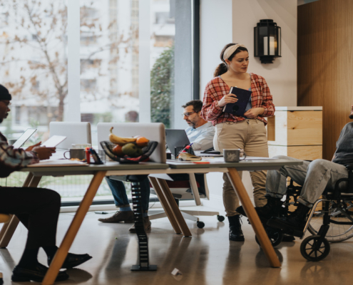 A diverse office team collaborates in an inclusive workspace, with one member in a wheelchair using a laptop.