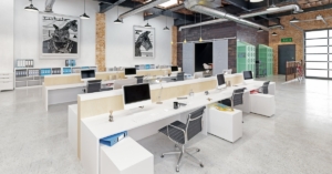 Sunlight filling a modern loft. The space has brick walls, tall windows, two hanging paintings, and minimalist furniture.