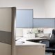 A black leather empty chair waits at tidy desk in cubicle that has blue shelves and white folder organizers.