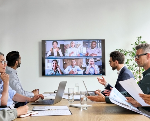 A group of diverse company employees having an online business conference video call in a board meeting room.