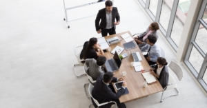 A top view of group of busy people working in an office, sitting around a conference table with notebooks and laptops.