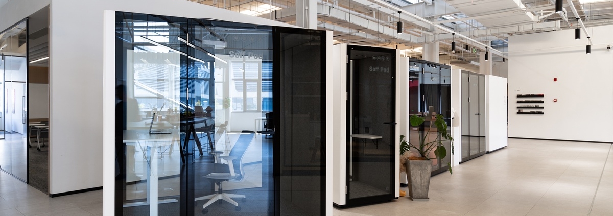 A close-up of multiple modern offices with glass-enclosed privacy pods and bright lighting within a large warehouse.