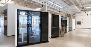A close-up of multiple modern offices with glass-enclosed privacy pods and bright lighting within a large warehouse.