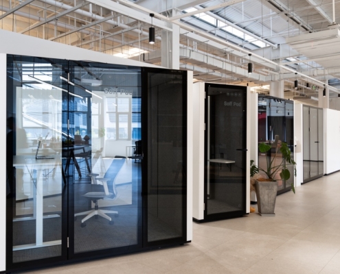 A close-up of multiple modern offices with glass-enclosed privacy pods and bright lighting within a large warehouse.