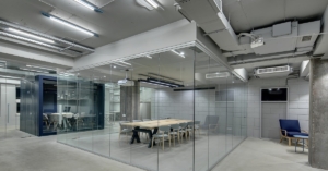 A bright loft-style meeting area is divided by glass partitions, with glowing lamps and gray brick walls.