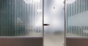 A view behind the frost, a glimpse into room two's serene spaces, framed by elegant stripes in a modern office.