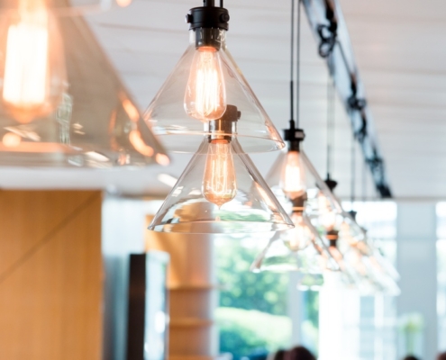A close-up of a row of yellow-toned, glass industrial-styled hanging ceiling lights in a modern shared office space.