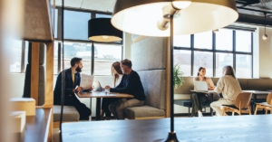 Businesspeople working a modern office building with privacy study booths and a large sectional couch for employees.