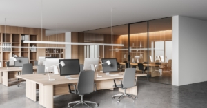 Bright open-plan office with wood shelving, grouped desks and monitors, and glass conference room enclosure.