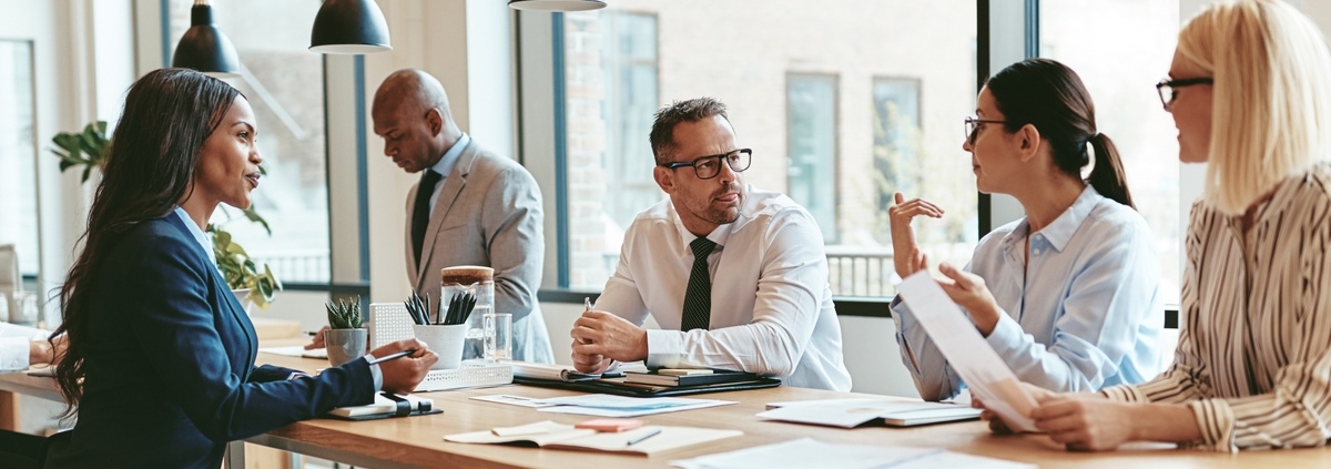 A diverse group of businesspeople talking together in a modern company conference table around an office table.