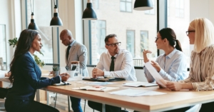 A diverse group of businesspeople talking together in a modern company conference table around an office table.