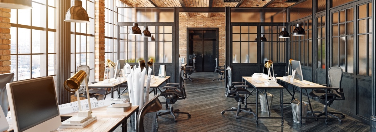 Open-plan loft office featuring exposed brick, glass partitions, wood flooring, and workstations with computers.