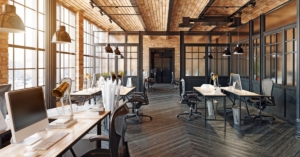 Open-plan loft office featuring exposed brick, glass partitions, wood flooring, and workstations with computers.