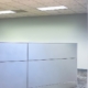 Empty office cubicles with gray partitions, patterned carpet, and drop ceiling lights in a quiet workspace.