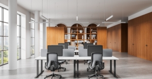 Contemporary workspace with shared desks, computer screens, office chairs, and built-in wooden cabinets and bookshelves.