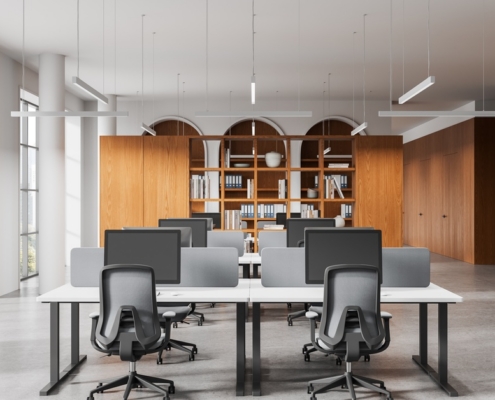 Contemporary workspace with shared desks, computer screens, office chairs, and built-in wooden cabinets and bookshelves.