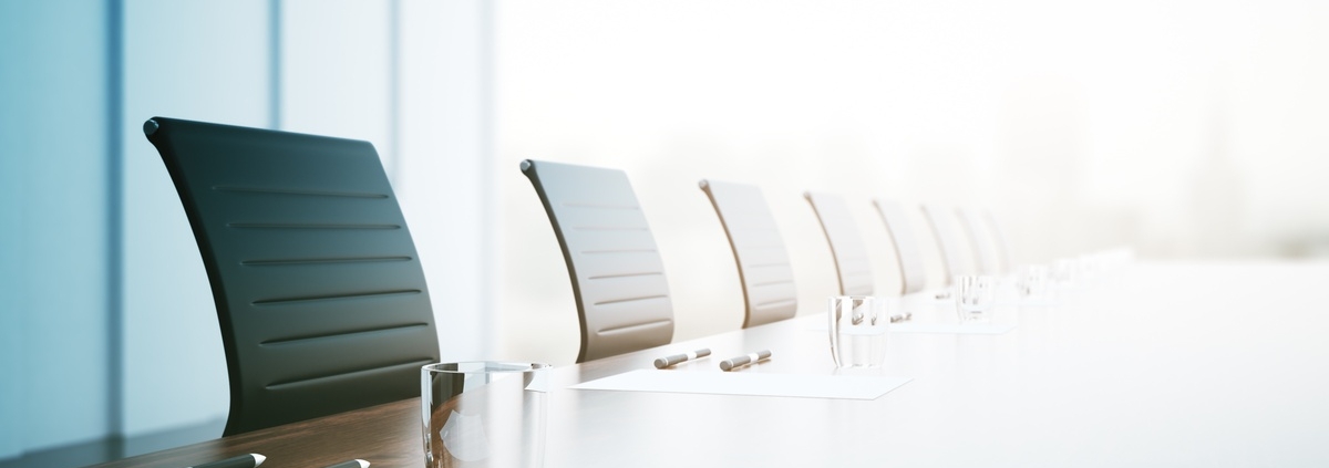 Bright conference room with a long table, empty chairs, glasses, pens, and papers lined up for a meeting.