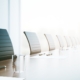 Bright conference room with a long table, empty chairs, glasses, pens, and papers lined up for a meeting.