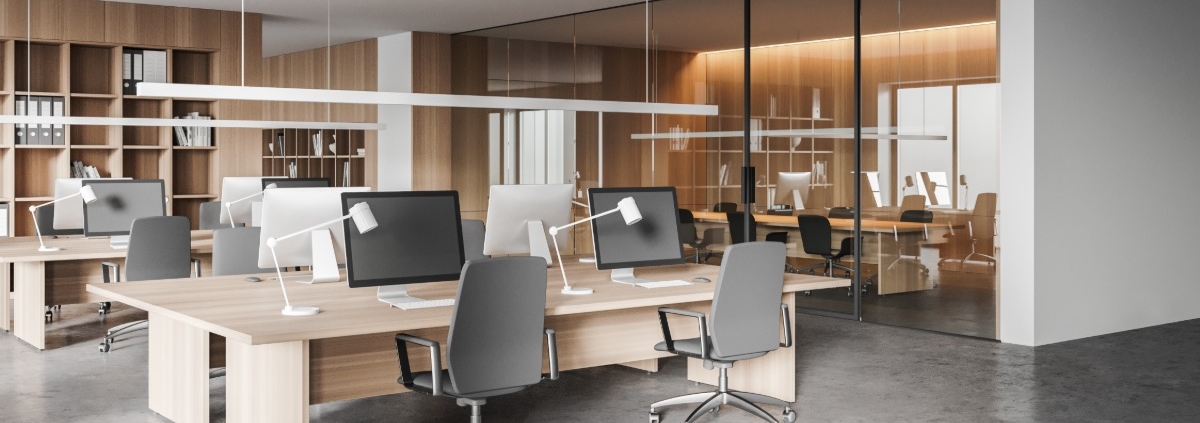 Modern open office with shared desks, computer monitors, task lamps, rolling chairs, and glass-walled meeting rooms.