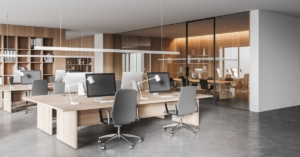 Modern open office with shared desks, computer monitors, task lamps, rolling chairs, and glass-walled meeting rooms.