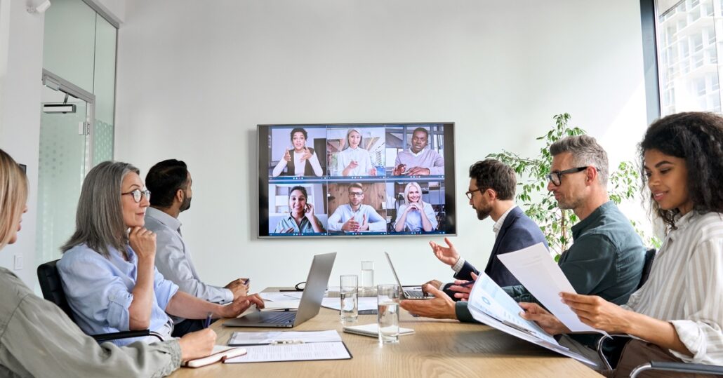 A group of diverse company employees having an online business conference video call in a board meeting room.
